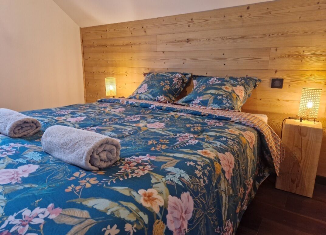 A bedroom with a wooden headboard, floral bedding, two rolled towels, and bedside lamps.