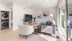 Ein modernes Wohnzimmer mit Flachbildfernseher, einer Couch, einem Couchtisch und einer Essecke mit Holztisch und Stühlen.
