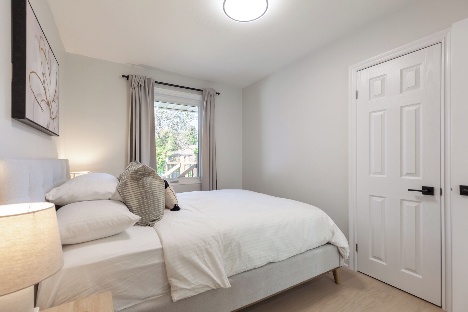 Ein Schlafzimmer mit einem Bett, einer Nachttischlampe, einem Fenster mit Vorhängen und einer Tür.