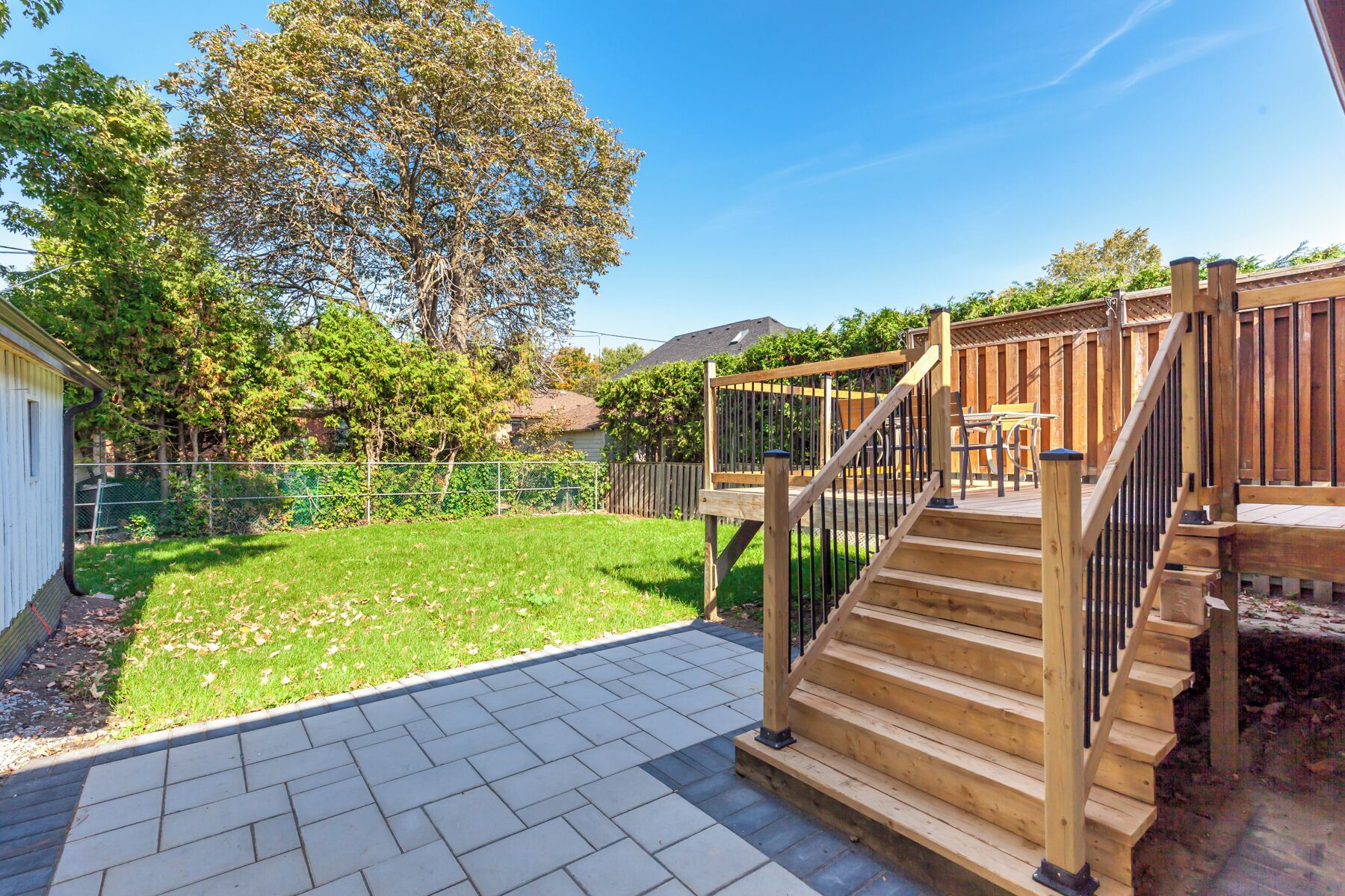 A backyard with a wooden deck, a staircase, and a fenced area.