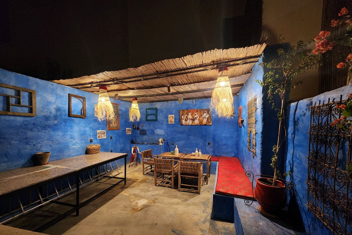 A room with a blue wall, a wooden table, a red bench, and hanging lights.