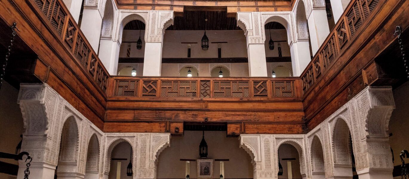 Un interior con balcón de madera, arcos blancos y faroles colgantes.