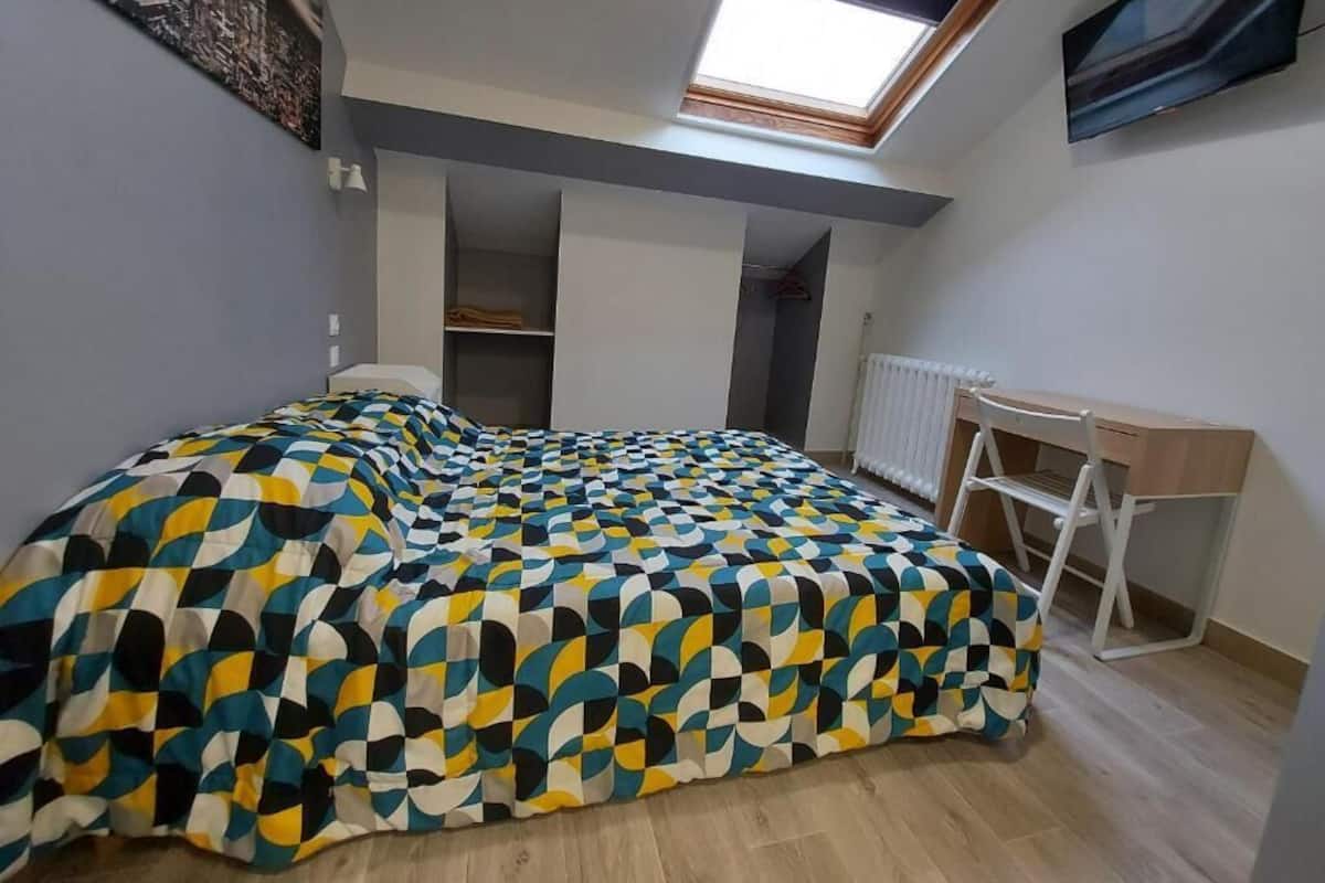 Un dormitorio con cama, escritorio, silla, radiador y tragaluz.