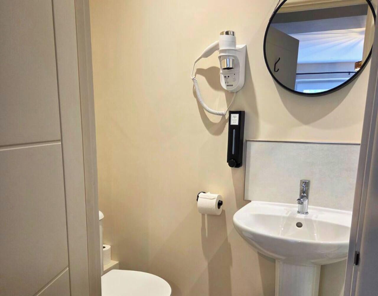 A bathroom with a toilet, a sink, a mirror, and a hairdryer on the wall.