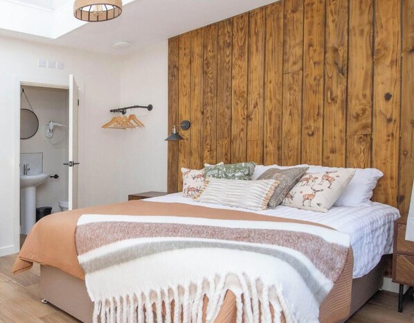 Un dormitorio con cabecera de madera, una cama con muchos cojines, una mesita de noche y una lámpara colgante.