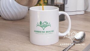 A hand pouring coffee into a mug with the Ashdene House logo. - The Distinguished Squirrel - Room 4 - New Forest (Dibden Purlieu)