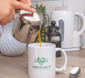 Una mano vertiendo café en una taza con el logo de Ashdene House.