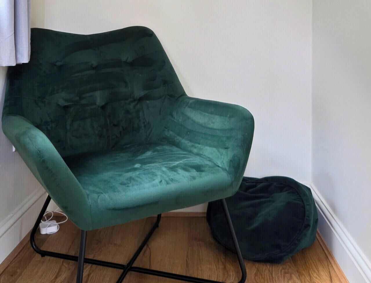 A teal armchair with a cushioned seat and backrest, positioned on a wooden floor against a white wall.