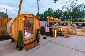 A wooden cabin with a glass door, a small outdoor seating area with chairs, and a staircase leading to a deck. - Southern Retreat • Pool, Hot Tub & Games • Near DT (Greenville)