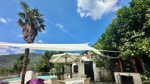 An outdoor patio with a pool, wooden furniture, and a white umbrella. - Villa with pool in a quiet hamlet among olive groves 8 km from the sea. (Chiusanico)