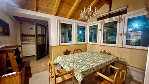 A dining area with a wooden table and chairs, a chandelier, and a view through large windows. - Villa with pool in a quiet hamlet among olive groves 8 km from the sea. (Chiusanico)