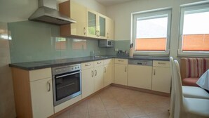 A compact kitchen with a stove, oven, microwave, and a window with blinds. - Vacation cottage Maric (Oetz)