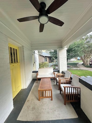 A covered porch with a ceiling fan, wooden furniture, and a yellow door.