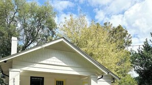 Uma casa térrea com fachada branca, varanda frontal e gramado bem cuidado.