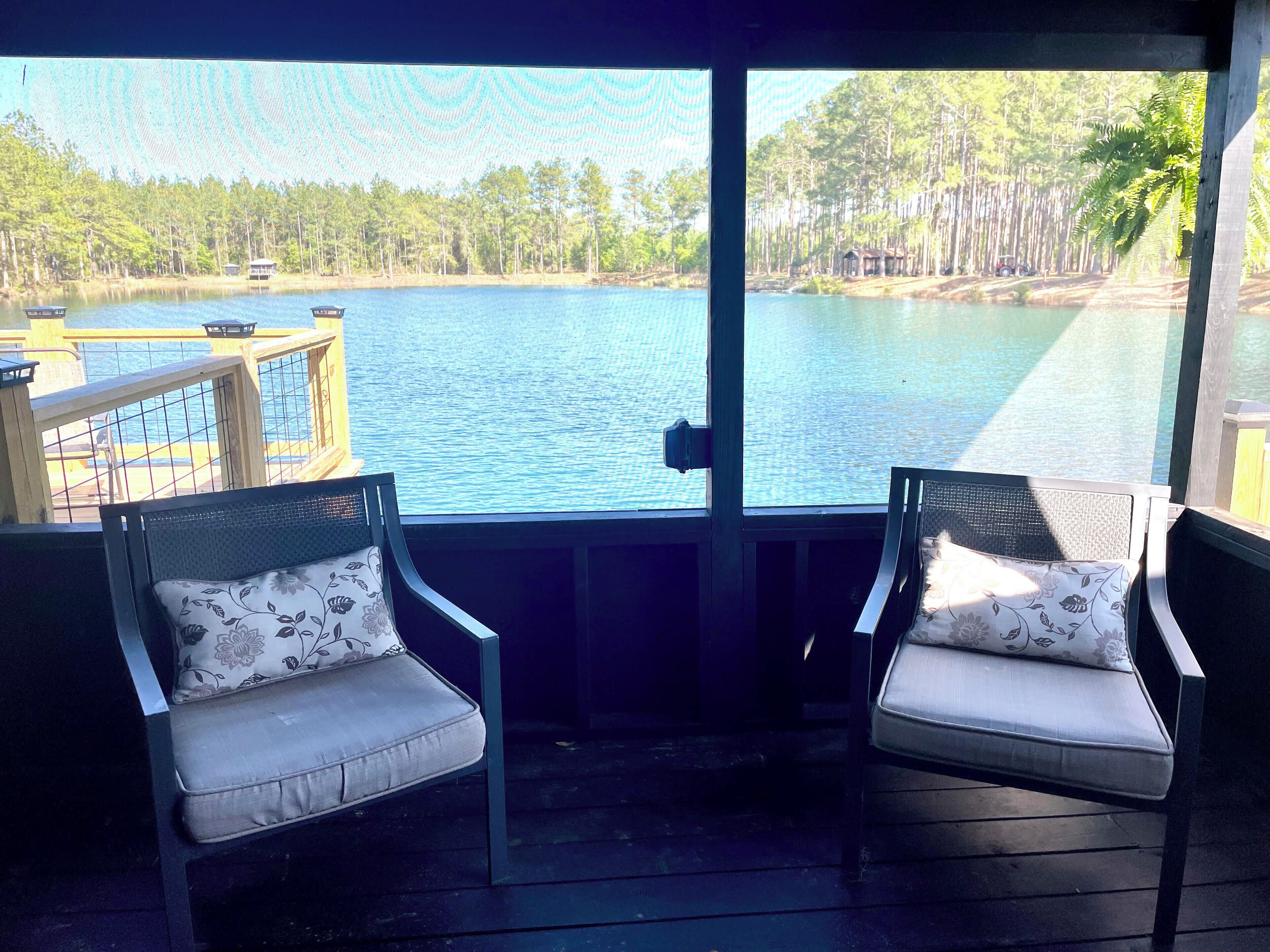 A covered outdoor seating area with two chairs and a view of a lake and forest.