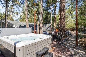 A hot tub in a forested area with a wooden deck and outdoor furniture.