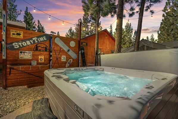 A wooden cabin with a hot tub, surrounded by trees and string lights.