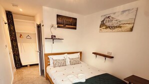A bedroom with a bed, a desk, a chair, a ceiling light, a painting, and a door.