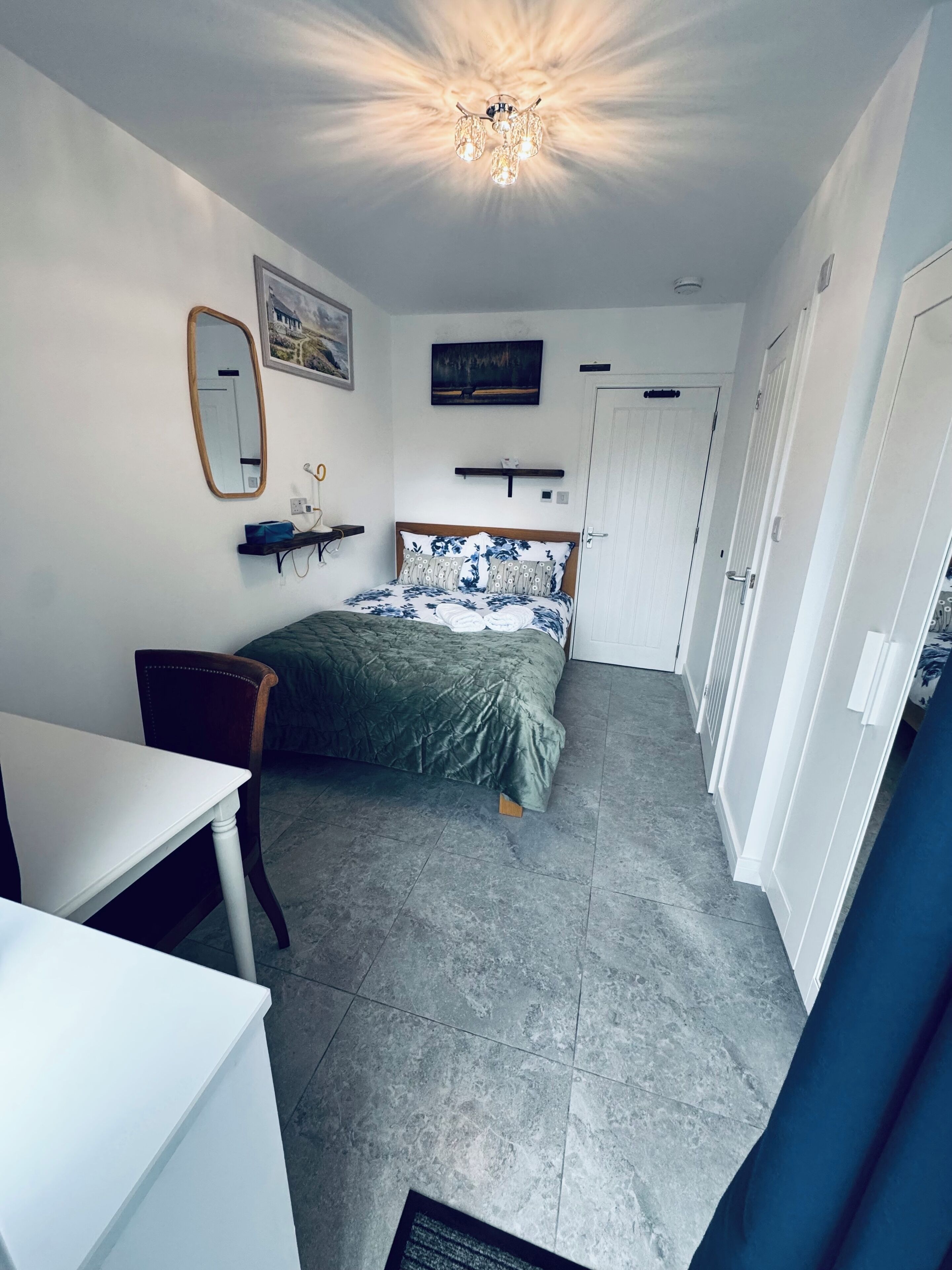 A bedroom with a bed, a desk, a chair, a mirror, and a ceiling light fixture.