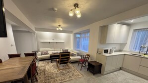 A modern living room with a wooden dining table, a sofa, and a kitchen area with a microwave and cabinets.
