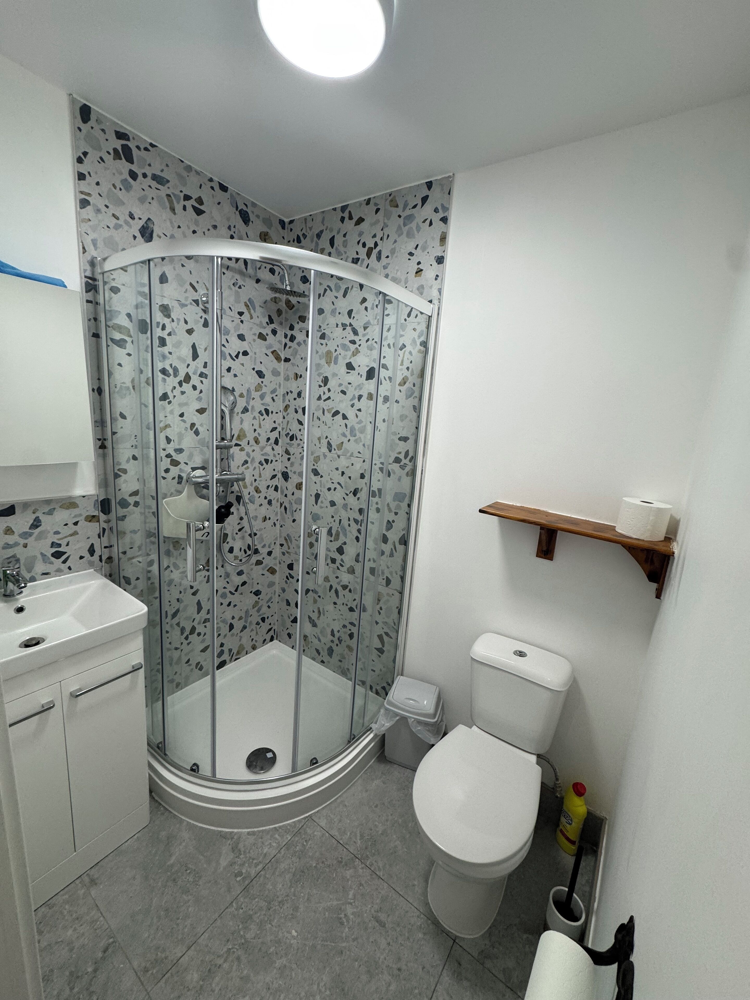 Un baño moderno con cabina de ducha de vidrio, inodoro blanco y lavabo con espejo.