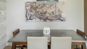 Un coin repas comprenant une table, deux chaises, une suspension et une œuvre d’art accrochée au mur.