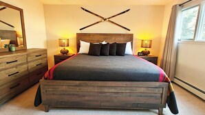 Une chambre à coucher avec un lit en bois, deux tables de chevet avec des lampes, une commode en bois et un grand miroir.