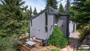 Une cabane moderne, de plain-pied, dotée d’une terrasse et d’un espace salon extérieur, et entourée d’une forêt dense.