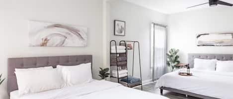 A hotel room with two beds, a ceiling fan, a wall-mounted artwork, a towel rack, and a potted plant.