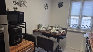 Eine kompakte Küche mit Mikrowelle, Backofen und einer Essecke für vier Personen, ausgestattet mit Tisch, Stühlen und einem Fenster mit Jalousien.