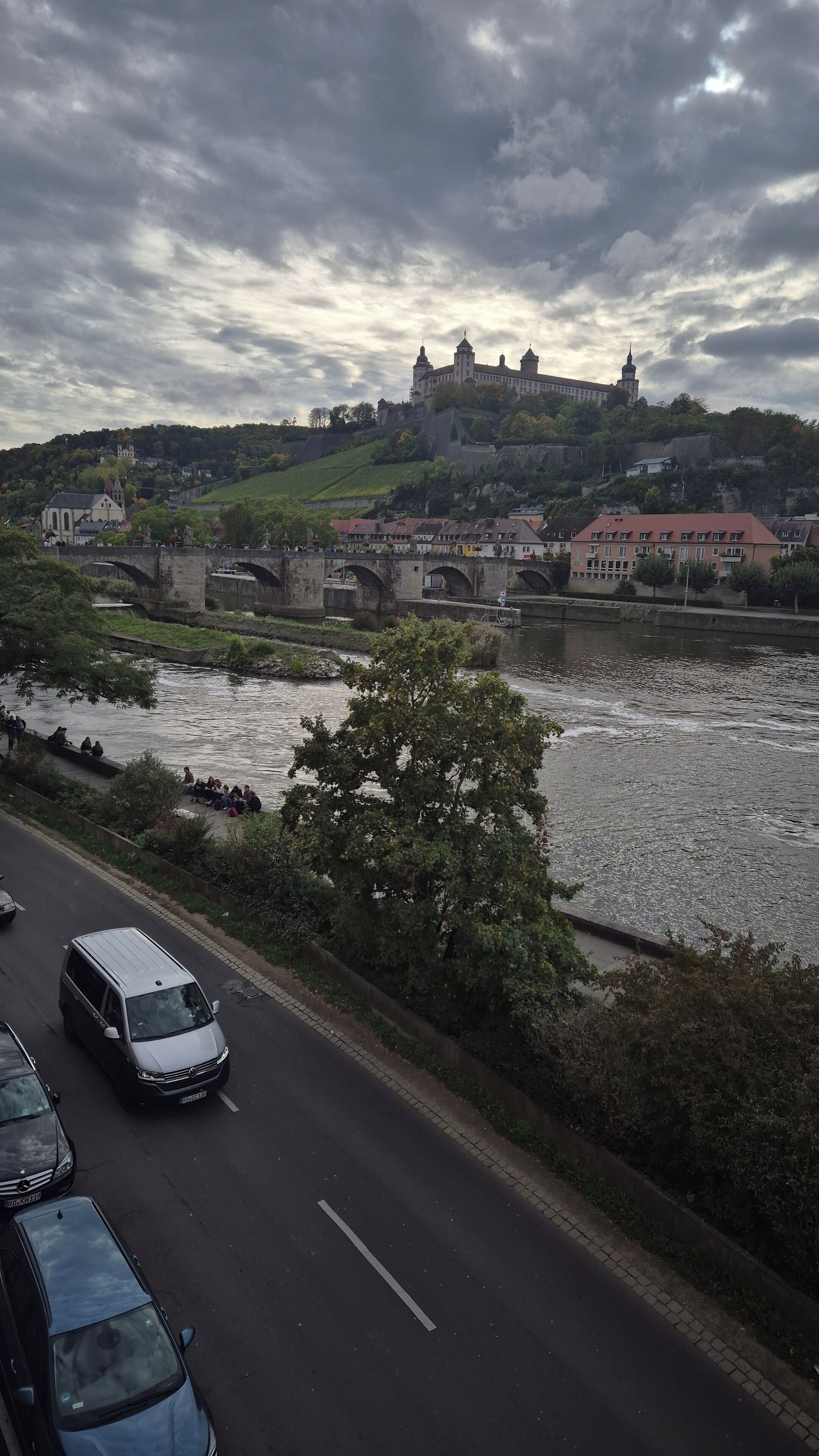 A river with a bridge, a castle on a hill, and vehicles on a road.