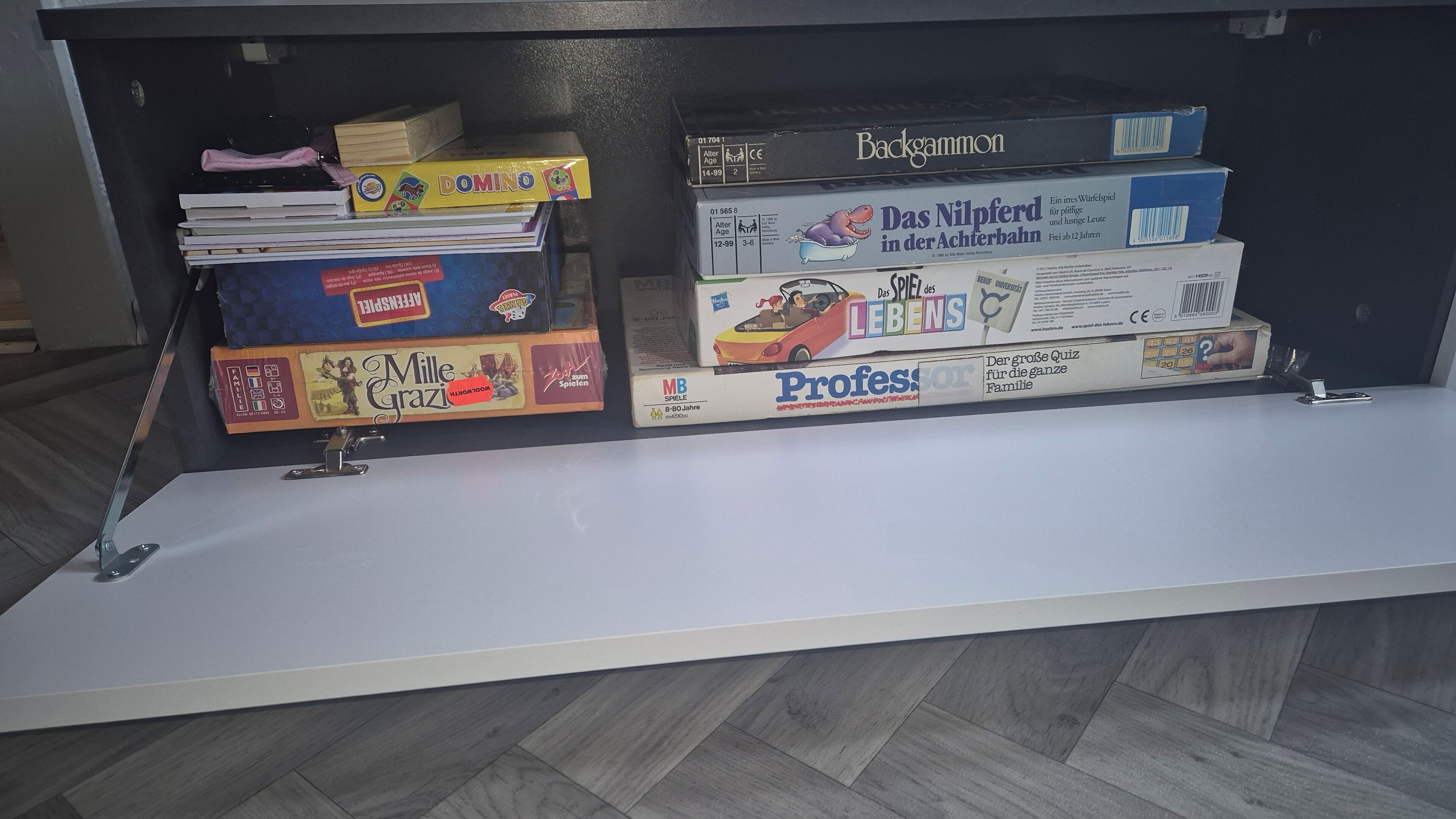 A shelf with various board games, including 'Domino', 'Mille Grazi', and 'Professors'.