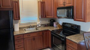 A kitchen with wooden cabinets, a black refrigerator, a stainless steel sink, a microwave, and an oven.