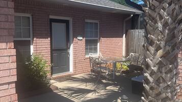 Un immeuble résidentiel avec une façade en briques, une porte d’entrée et un petit patio aménagé avec du mobilier d’extérieur.