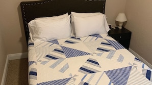 A bed with a patterned quilt, a dark headboard, and a bedside table with a lamp.