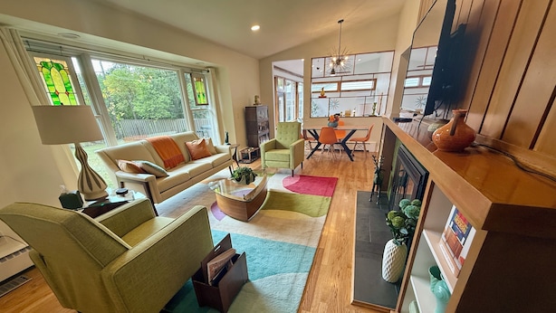 A spacious living room with a sofa, chairs, a coffee table, and a fireplace. There is a dining area with a table and chairs, and a TV mounted on the wall. - A2 Oasis; Lovely Neighborhood; Walk to Stadium and Crisler Arena! (Ann Arbor)