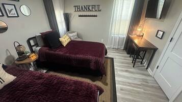 A bedroom with two beds, a bedside table, a wall clock, a mirror, and a 'THANKFUL' sign.
