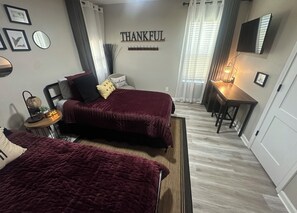 Een slaapkamer met twee bedden, een nachtkastje, een wandklok, een spiegel en een bord met de tekst 'THANKFUL'.
