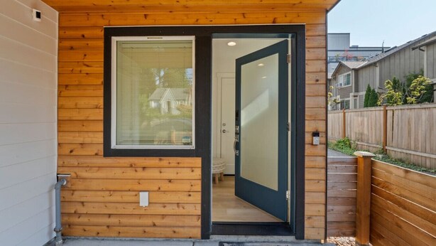 Fachada de madera con puerta de vidrio y felpudo.