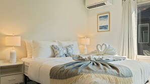 Habitación de hotel con una cama, dos mesitas de noche, una lámpara, aire acondicionado, un cuadro enmarcado y una ventana con cortinas.