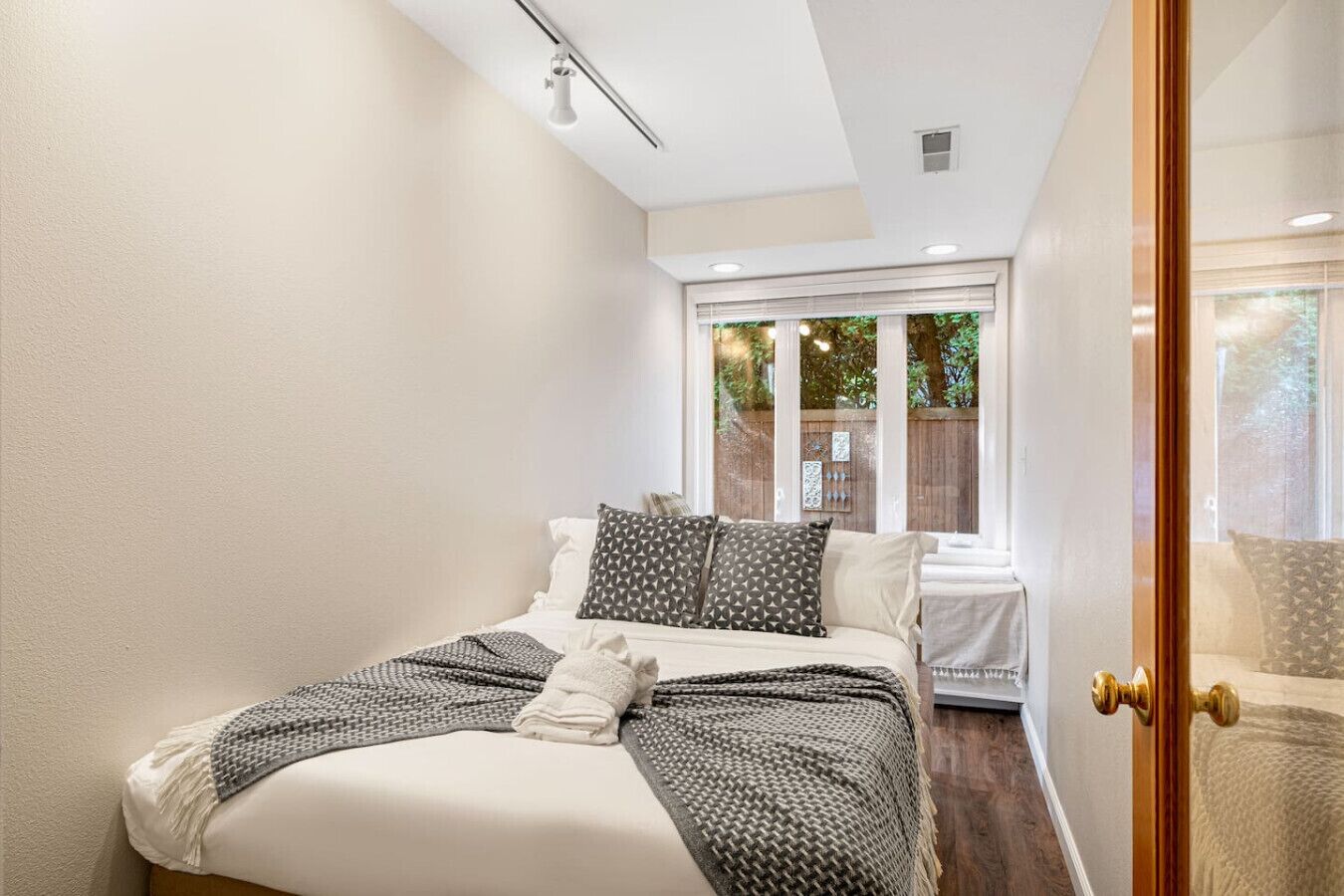 Une chambre à coucher avec un lit, des oreillers, une couverture, une fenêtre et une porte.