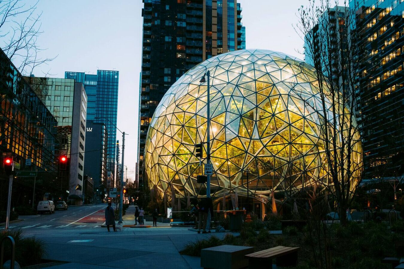 Una estructura esférica con un diseño geométrico, rodeada de edificios urbanos y una calle con gente caminando.