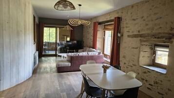 A room with a dining table, chairs, a sofa, and a TV in the background.