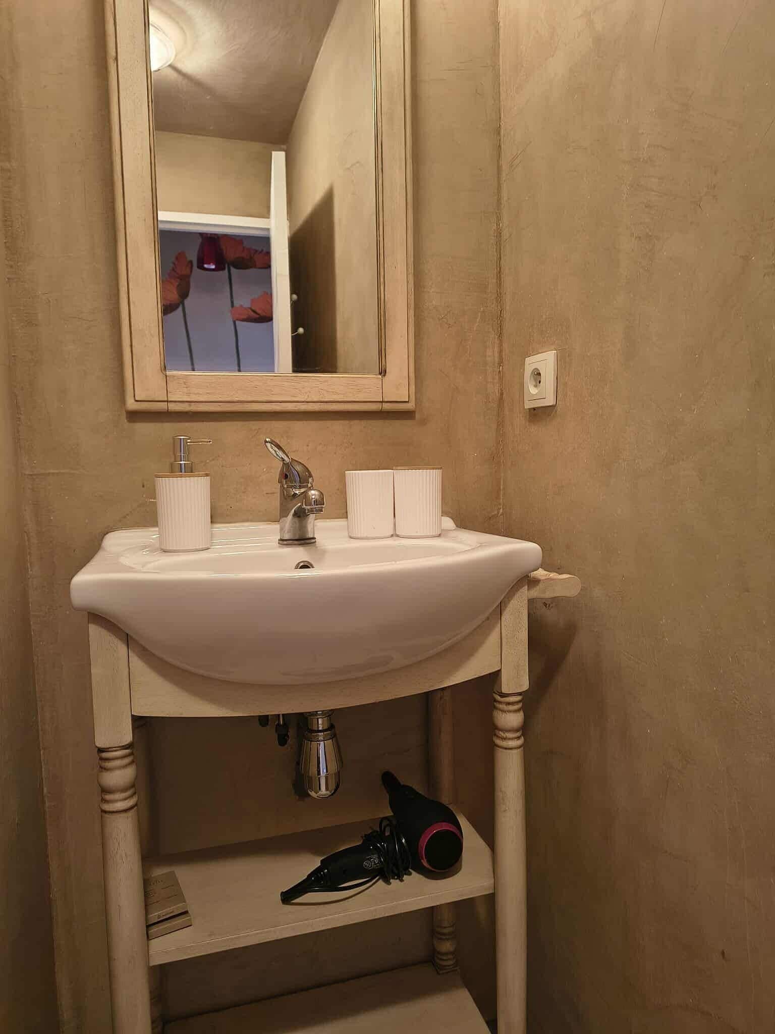 Een badkamer met een wit wastafel, een spiegel en een haardroger op de plank.