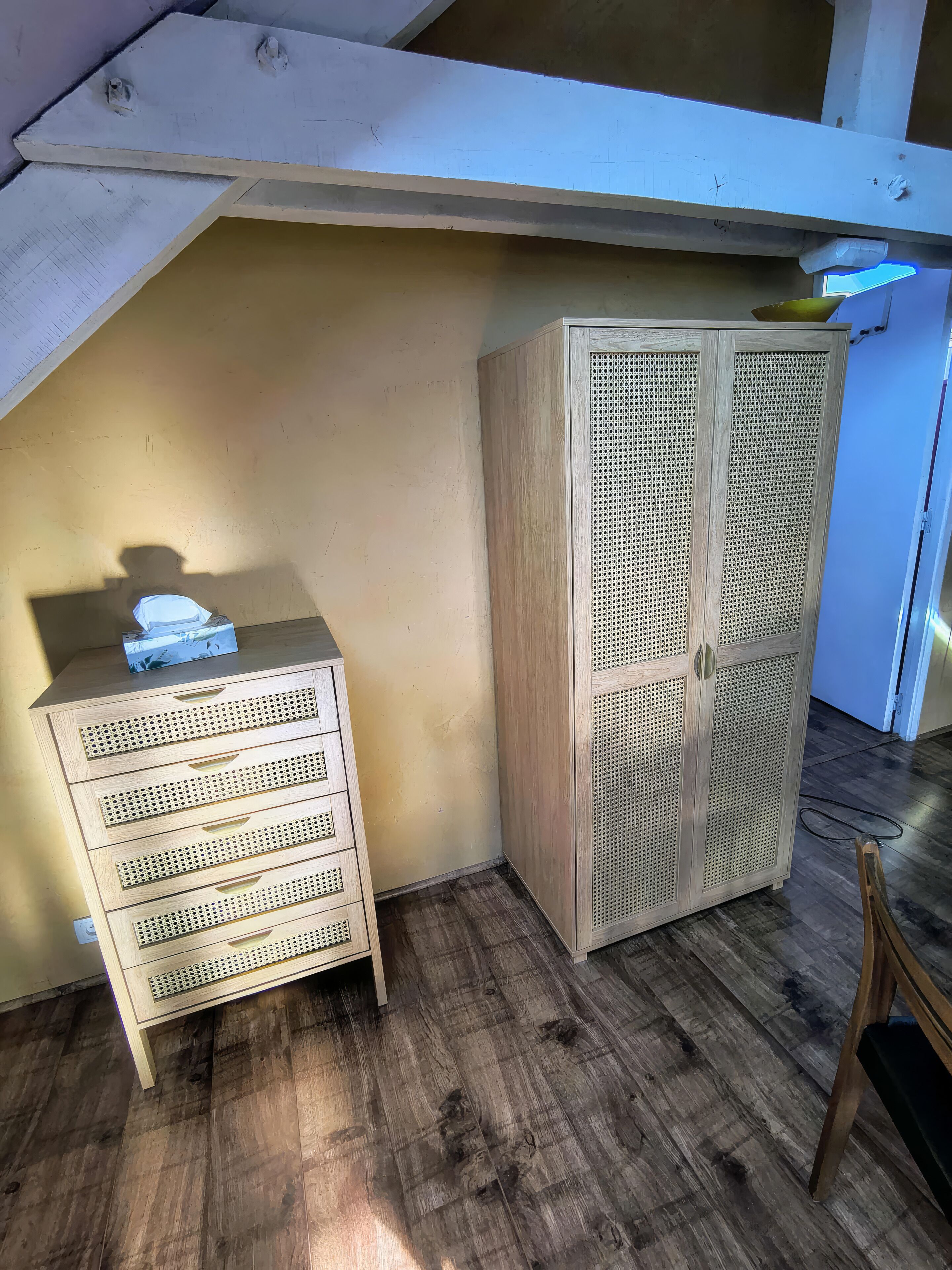 Une pièce comprenant un meuble en bois doté de portes perforées, une petite commode en bois et une chaise.