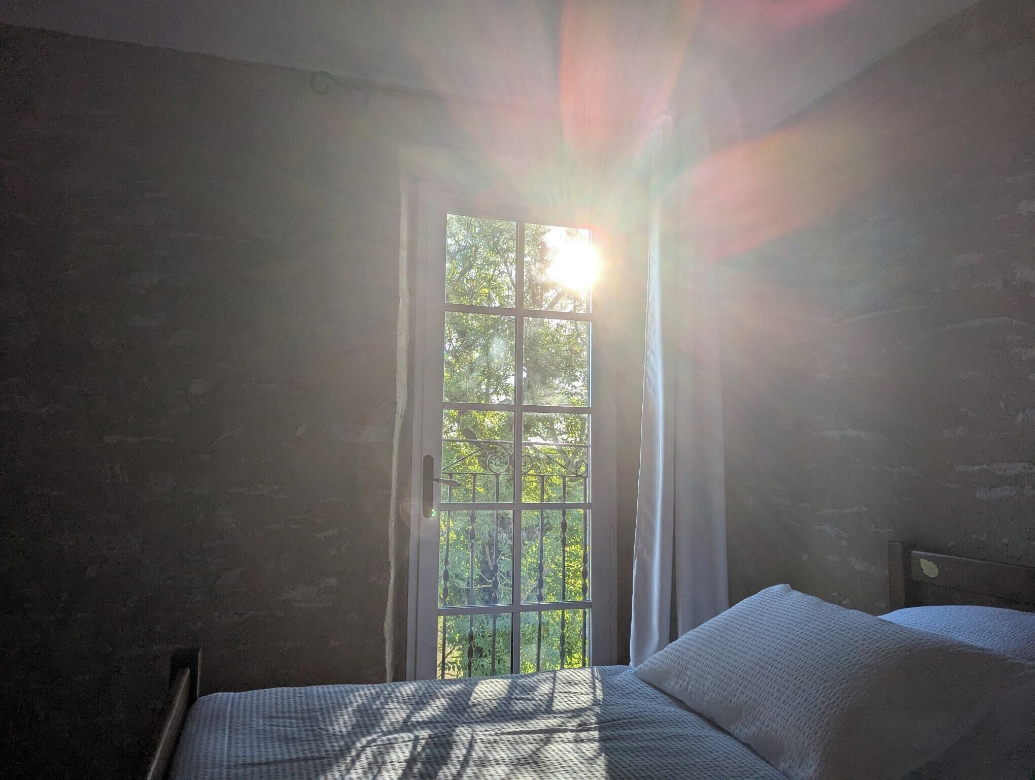 Een kamer met een bed, een raam met uitzicht op bomen en een gordijn.