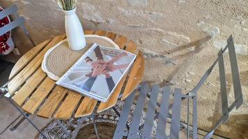 A round wooden table with a white vase of dried flowers and a magazine. A metal chair with a woven seat cushion is placed beside the table.