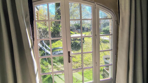A room with a large arched window, a wooden ceiling, and a doormat with a tree design. - Saisonnée (Centrès)