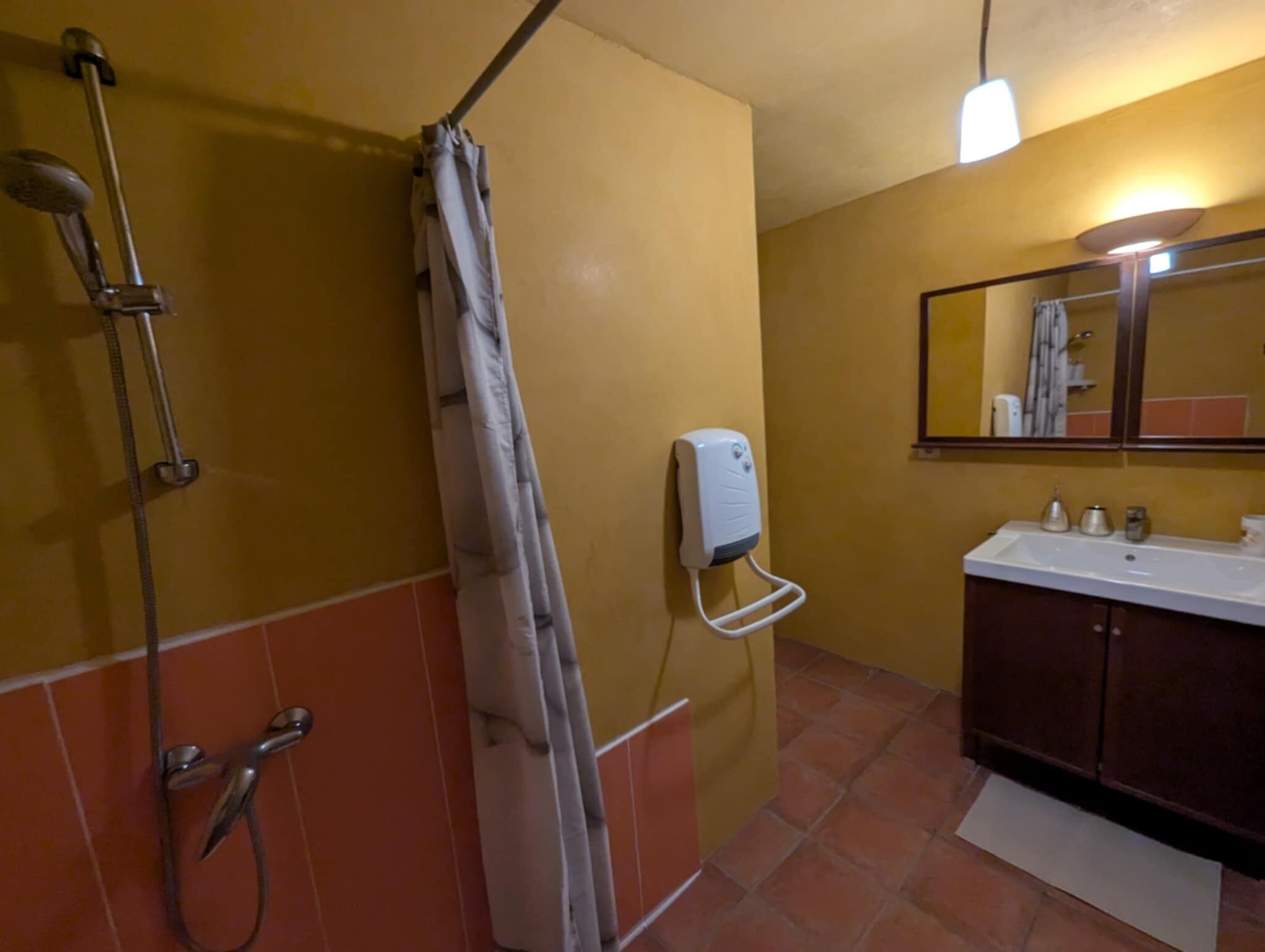 A bathroom with a shower, a hand dryer, a sink, and a mirror.