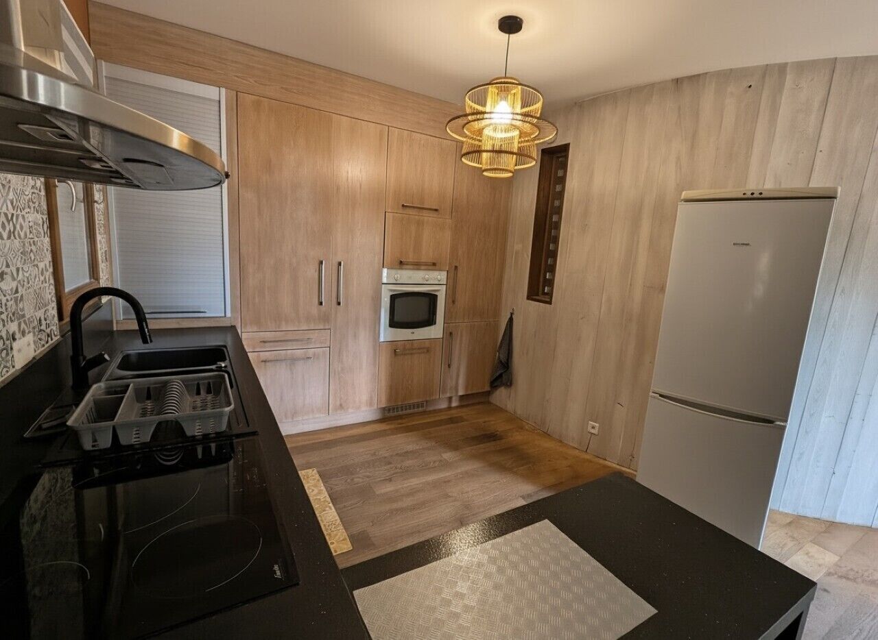 A kitchen with a black countertop, wooden cabinets, a built-in oven, a microwave, and a refrigerator.